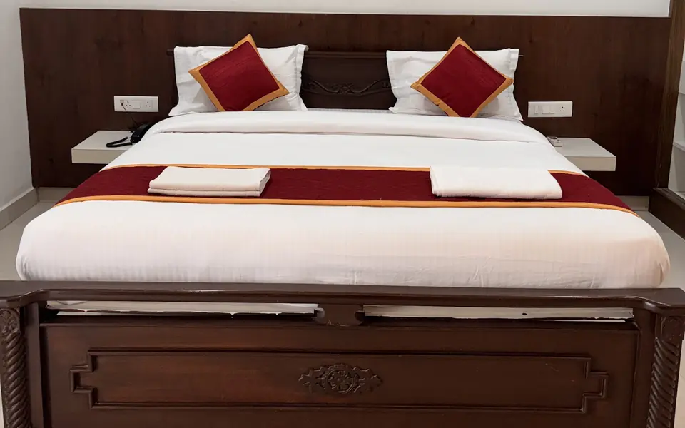 Delux Room bed with wooden headboard and crisp white linen at Arcade Stay Inn, Tirupati